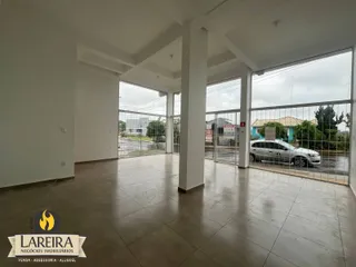 Interior de uma sala ampla com piso de cerâmica e grandes janelas que dão para o exterior.