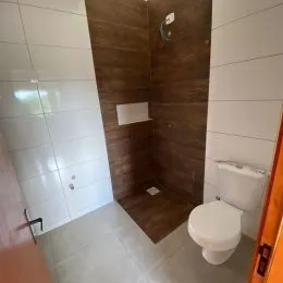 Interior de um banheiro com piso claro e área de box revestida em tons de marrom.
