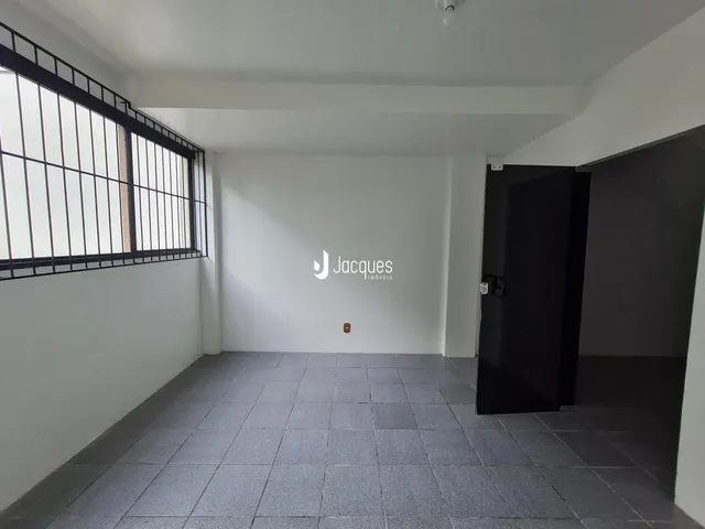 Vista interna de um corredor com piso de cerâmica cinza e janela de metal na parede esquerda.