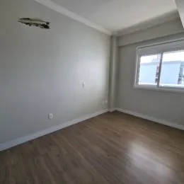 Foto interna de um cômodo com piso de madeira e paredes cinzas.