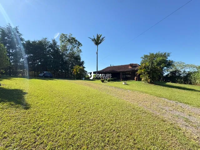 Vista externa de uma propriedade com grande área gramada e vegetação ao redor.