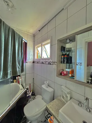 Foto interna de um banheiro com azulejos brancos e louças sanitárias brancas.