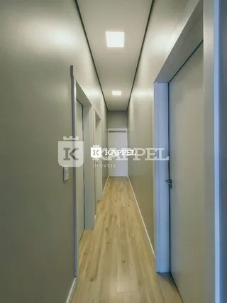 Foto de um corredor interno com piso de madeira clara e paredes claras.