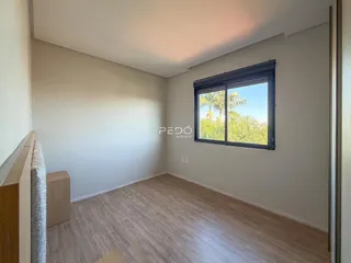 Ambiente interno de uma sala com piso de madeira clara e janela com vista para a vegetação.