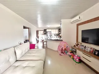 Foto da sala de estar com sofá branco e cozinha ao fundo.
