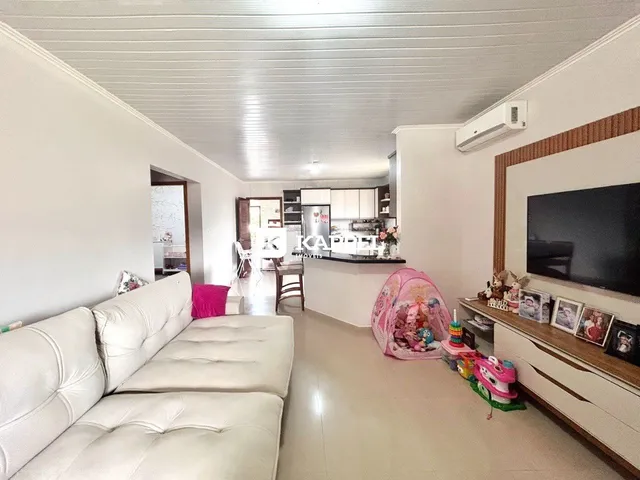 Foto da sala de estar com sofá branco e cozinha ao fundo.