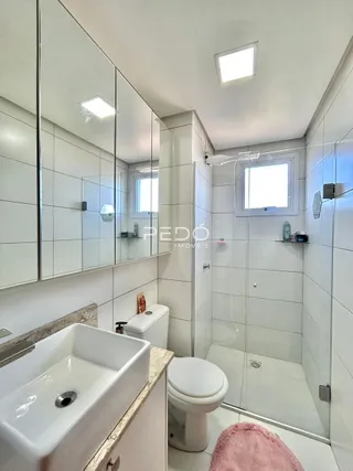 Interior de um banheiro com azulejos brancos e box de vidro.