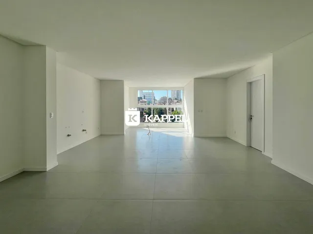 Vista interna de um ambiente amplo com piso claro e grande janela para a paisagem urbana.