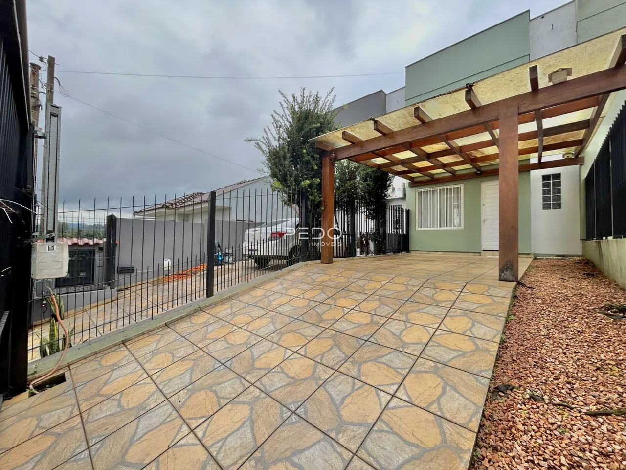 Área externa pavimentada com piso de cerâmica e cerca de ferro.