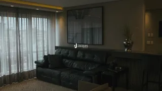 Sala de estar com sofá escuro e grandes janelas cobertas por cortinas.