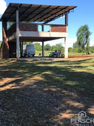 Vista externa de uma estrutura coberta com pilares de concreto em uma área gramada.