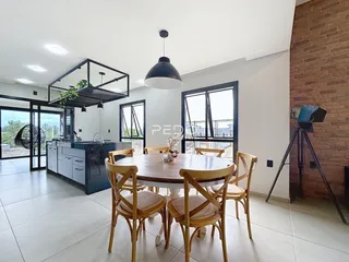 Ambiente interno de uma sala de jantar com cozinha aberta e grandes janelas.