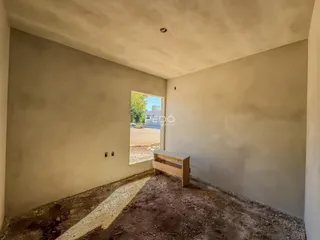 Interior de um cômodo com paredes em obra e piso de terra.