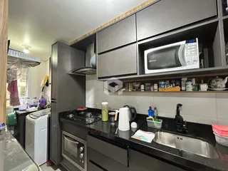 Vista interna de uma cozinha moderna com armários escuros e bancadas pretas.