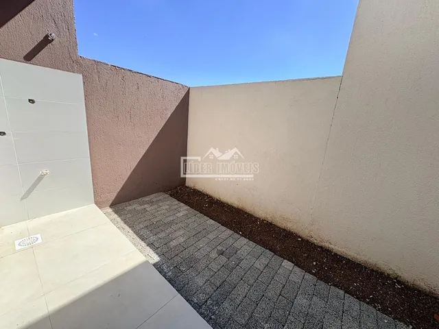 Vista externa de um pátio com paredes de cor clara e piso pavimentado.