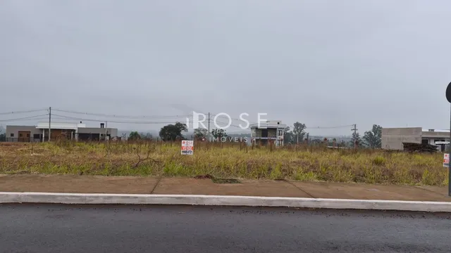 Vista externa de uma propriedade com vegetação seca e edifícios ao fundo.