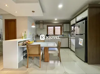 Cozinha moderna com bancadas brancas e mesa de jantar de madeira.