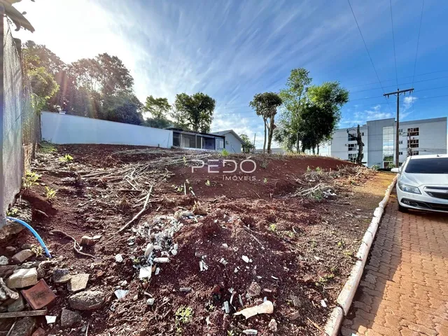 Vista externa de um terreno com terra exposta e vegetação no fundo.
