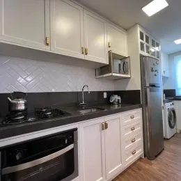 Cozinha com armários brancos e bancada escura em um imóvel.