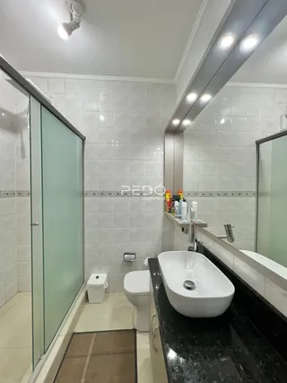 Um banheiro com revestimento cerâmico branco e box de vidro.