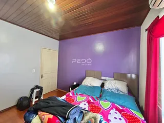 Quarto com cama e cabeceira em ambiente com teto de madeira.