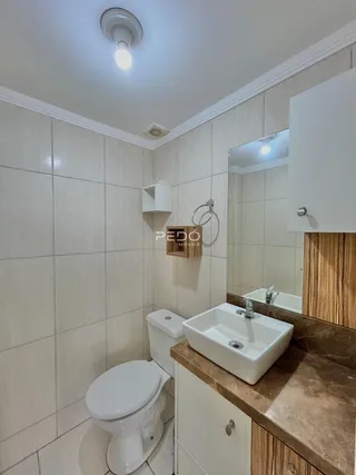 Banheiro com revestimento de cerâmica branca e bancada de pedra marrom.