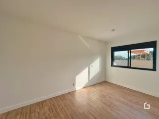 Interior de uma sala de estar com piso de madeira clara e grande janela.