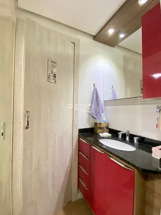 Vista de um corredor com porta branca e reflexo de um banheiro com bancada escura.
