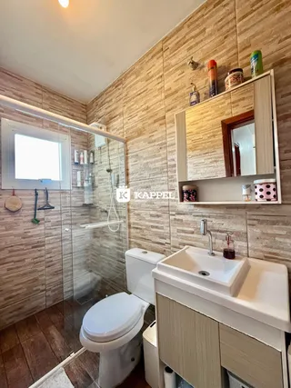 Banheiro com box de vidro, vaso sanitário e bancada de pia.