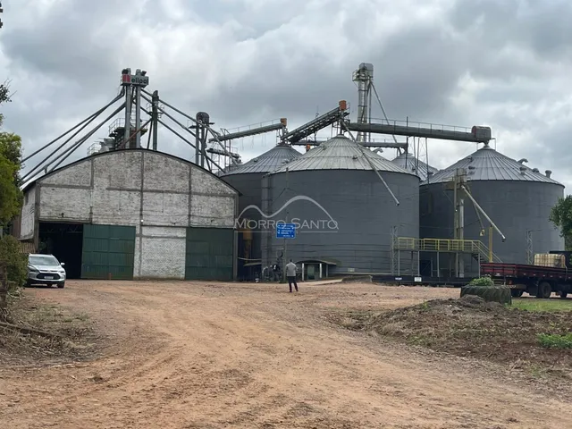 Foto de silos industriais e um galpão em uma área de terra.