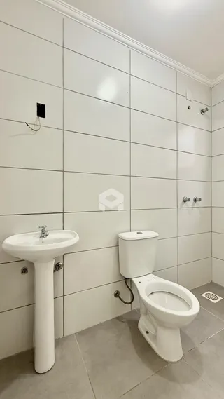 Foto de um banheiro com pia e vaso sanitário em paredes brancas.