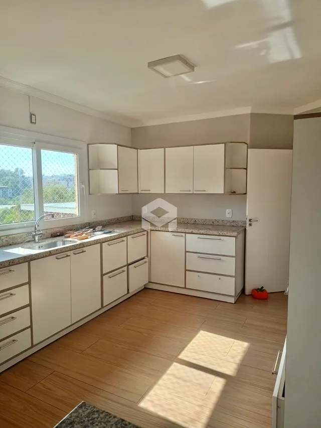Vista interna de uma cozinha com armários brancos e piso de madeira.