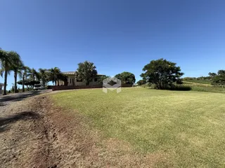 Vista externa de uma propriedade com gramado e árvores sob um céu azul.