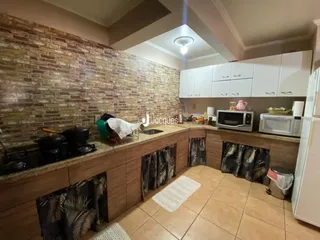 Vista da cozinha com parede de tijolos aparentes e armários brancos.