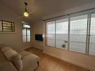 Sala de estar com piso de madeira e grandes janelas que dão vista para o exterior.