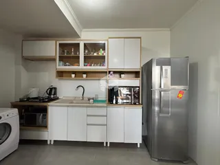 Vista interna de uma cozinha com armários brancos e prateleiras de madeira.