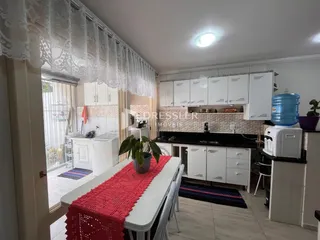 Uma cozinha com armários brancos e bancadas escuras é visível na imagem.