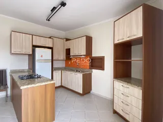 Vista da cozinha e sala de jantar com armários de madeira e piso cerâmico.