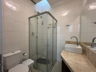 Banheiro com box de vidro, vaso sanitário e bancada de granito.