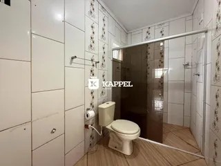 Banheiro com revestimento de azulejos brancos e box de vidro transparente.