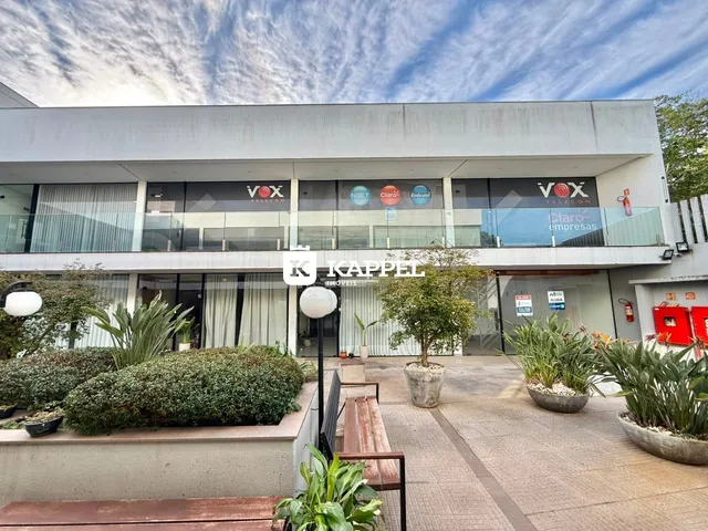 Fachada de um prédio comercial com grandes janelas e paisagismo na entrada.
