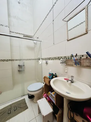 Foto interna de um banheiro com azulejos brancos e box de vidro.