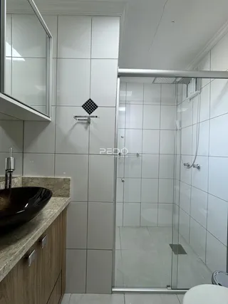 Foto de um banheiro com box de vidro e revestimento cerâmico.