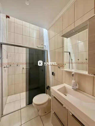 Banheiro com revestimento de cerâmica e box de vidro.