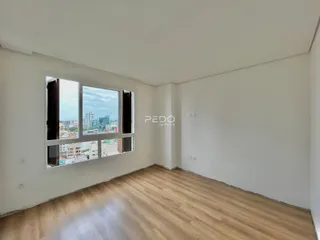 Ambiente interno com piso de madeira e janela com vista da cidade.
