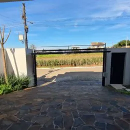 Vista da entrada da propriedade com portão metálico e pavimento de pedra.