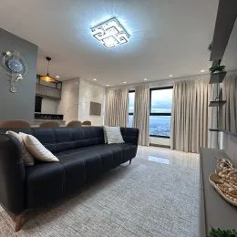 Foto interna de uma sala de estar com sofá escuro e piso claro.