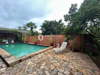 Piscina externa cercada por um muro de tijolos e área pavimentada.