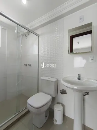 Foto interna de um banheiro com box de vidro, vaso sanitário e pia brancos.