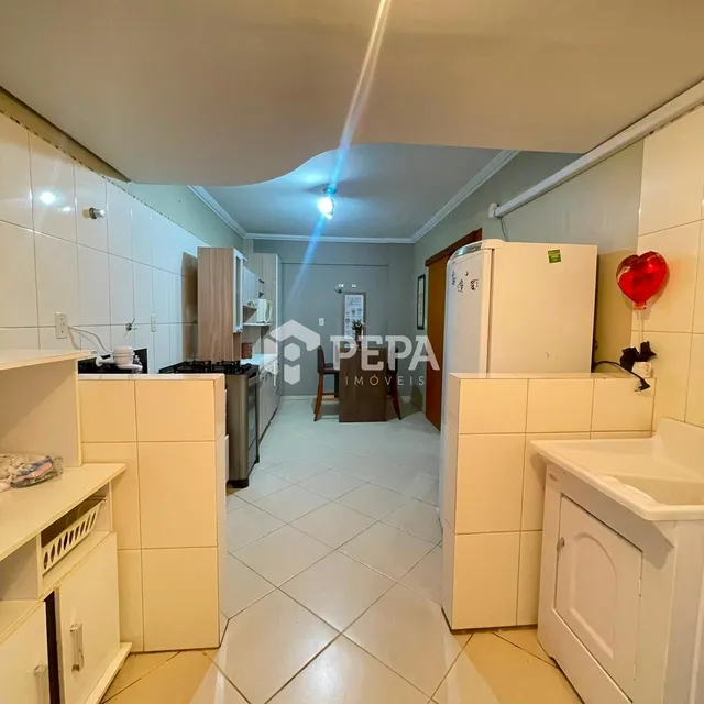 Foto interna de uma cozinha com revestimento branco e piso claro.